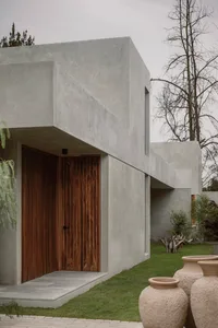 A modern house with a concrete exterior, featuring a wooden door and a landscaped garden with large ceramic pots.