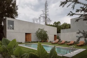 A modern residential exterior featuring a concrete wall, green lawn, and a swimming pool with lounge chairs.