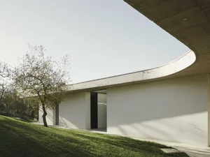 Modern residential building with curved concrete walls and a sloped lawn.