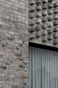 Grey brick wall with protruding elements and a window with sheer curtains.