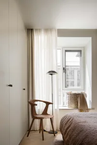 A minimalist bedroom featuring wooden furniture and a floor lamp.