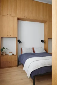 A minimalist bedroom featuring wood cabinets and a comfortable bed, designed for modern living.