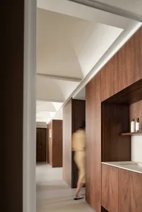 A minimalist corridor with wooden walls and a white ceiling. A person is seen entering a doorway in the background.