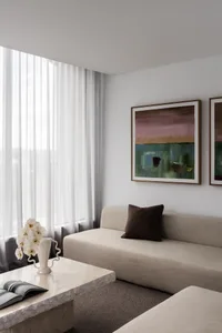 Modern minimalist living room with neutral tones, upholstered furniture, and abstract artwork.