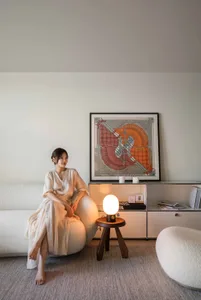 A woman sitting on a modern, white, soft chair in a minimalist living room setting.