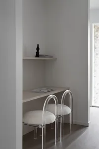 Minimalist interior design featuring transparent acrylic chairs, white upholstered seats, and light grey wooden surfaces.