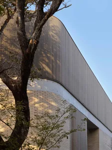 A modern building with a curved metal exterior and tree branches in the foreground.