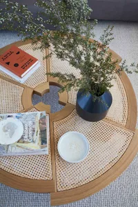 A modern coffee table with wood and cane design features, including a vase, books, and a bowl.