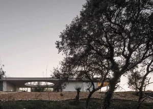 A modern, minimalist concrete house with a circular window and a natural landscape.