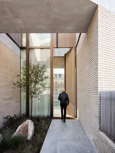 A modern entrance with a small garden and a cement path leading to wooden doors.