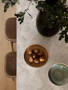 A modern kitchen counter made of marble with a bowl of pears and a green ceramic bowl.
