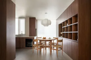 Modern residential kitchen featuring wooden furniture, a round dining table with chairs, and a large window with blinds.