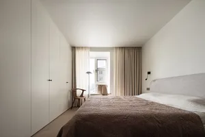 A minimalist bedroom with neutral-toned furniture and a window.