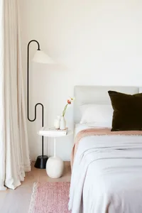 A modern minimalist bedroom features a bed with a upholstered headboard, a pink rug, and a side table with a vase of flowers.