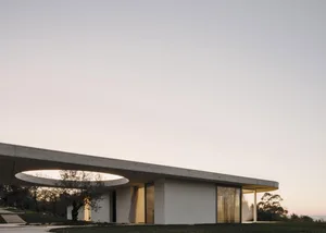 A sleek, modern minimalist house with a circular cut-out in the concrete roof, providing natural light to the interior. 