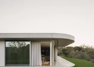 A modern minimalist house featuring a curved concrete roof and large glass windows.