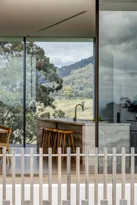 A modern minimalist kitchen with a concrete countertop and a view of lush green hills through large windows.