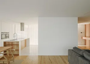 A minimalist living room featuring white walls, wooden furniture, marble flooring, and metallic accents.