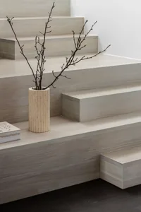 A minimalist interior featuring sleek, wooden stairs with a vase of twigs on the landing.