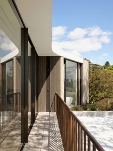 A modern residential exterior features a glass and wooden pool deck overlooking a bathroom interior.