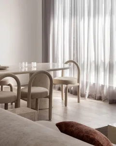 Modern minimalist dining room featuring a sleek marble table, plush fabric chairs, and wooden flooring.