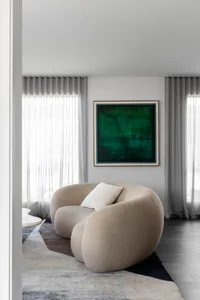 Modern minimalist living room with a fabric couch, green abstract painting, and grey curtains.