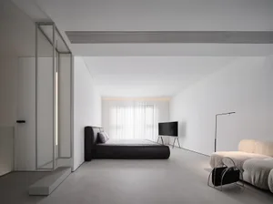 A minimalist bedroom featuring a black bed, a white couch, and concrete flooring, with a floor lamp and a television in the b