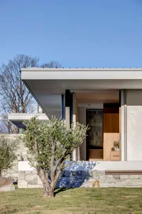 A modern residential exterior featuring stone walls, glass windows, and wooden elements.
