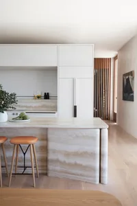 A modern residential kitchen with a white marble countertop, wooden stools, and a sleek white cabinet.