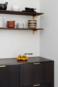 Modern storage cabinet with wooden finish and brass accents containing bowls and other items.
