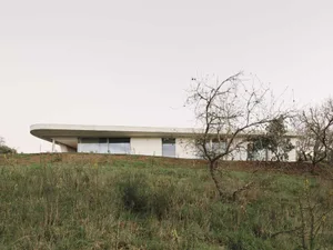 A modern house with a flat concrete roof and large windows on a grassy hillside.