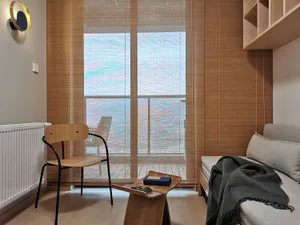 A modern minimalist living space featuring a large window with textured curtains, showcasing a view of the sea and a deck out