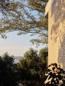 Modern brick building exterior with foliage and trees in the foreground.