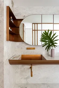 A modern bathroom with a marble sink and countertop, featuring a round mirror, open shelving, and a potted plant.