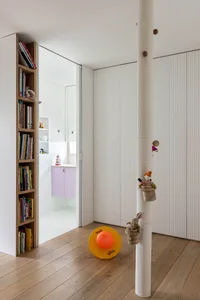 A modern children's room with white paneled walls, wooden shelves containing books and toys, and a wooden floor.