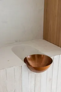 A modern, minimalist copper bowl placed on a white, textured counter surface.