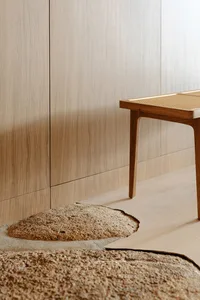 A wooden bench with a woven top, placed in a minimalist indoor setting.