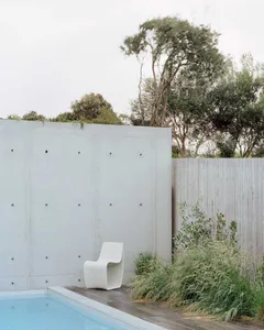 Modern interior with a concrete wall and white chair beside a pool.