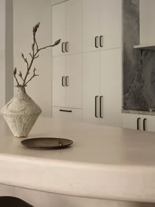 A modern kitchen features a concrete countertop with a minimalist vase and plate as decorative elements.