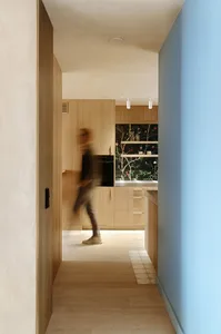A person walking in a modern kitchen with wooden cabinets and a blue wall.