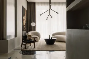 A modern living room with neutral-colored furniture, a round coffee table, and a minimalistic chandelier hanging above the se