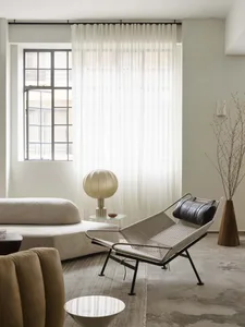 Modern living room featuring a minimalist design with a concrete floor, a beige sofa, a lounge chair with a black pillow, and