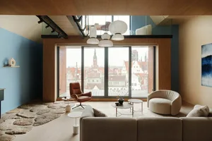 A modern living room with a wood floor, a large window, a leather armchair, and a beige sofa.