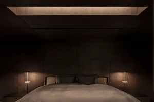 A minimalist bedroom with dark wooden walls and a bed with simple bedding.