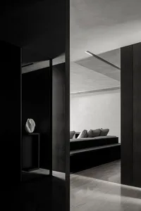 A modern minimalist living room with concrete walls, a built-in sofa, and a minimalist vase on a side table.