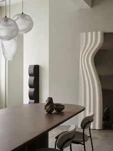 Modern minimalist dining room with a wooden table adorned with decorative vases and contemporary pendant lights.