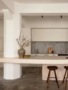 Modern minimalist kitchen with concrete accents and white cabinets, featuring a sleek countertop and minimalist decor.