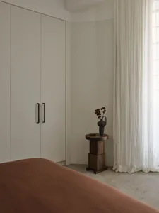 Minimalist bedroom featuring a textured bed, white curtains, and a white wardrobe with black handles.