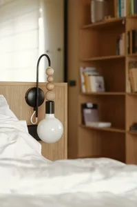 Minimalist bedroom features a white bed with wooden headboard and metal light fixture, surrounded by a bookshelf filled with