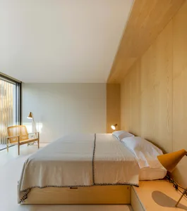 Modern minimalist bedroom with wooden walls and furniture, featuring a bed with a wooden headboard and matching bedside table